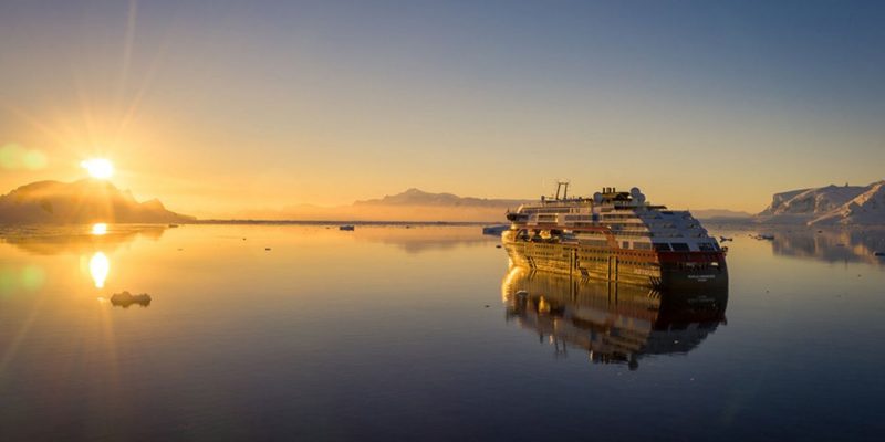 Een Hurtigrutenschip bij de ondergaande zon op exploratiereis met Nordic